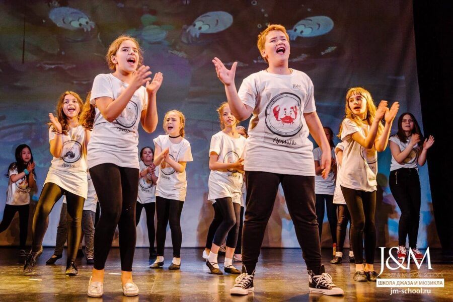 Дети в ярких театральных костюмах выступают на профессиональной сцене J&M C.A.M.P.
