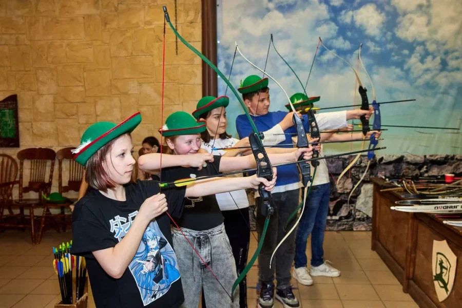 Стрелок в процессе натягивания тетивы арбалета, целится в мишень в клубе Шервуд