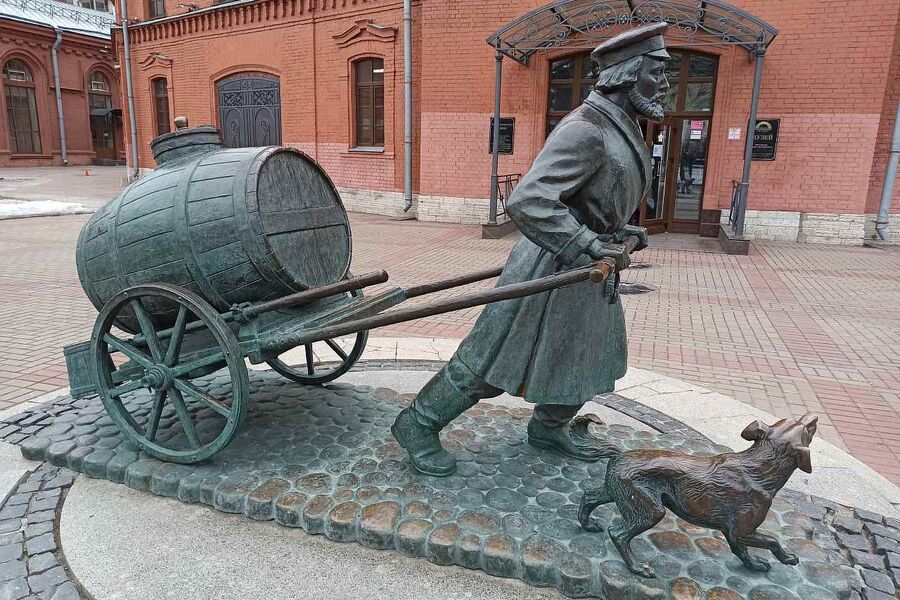 Бронзовая скульптура водовоза с бочкой воды у старинной водонапорной башни