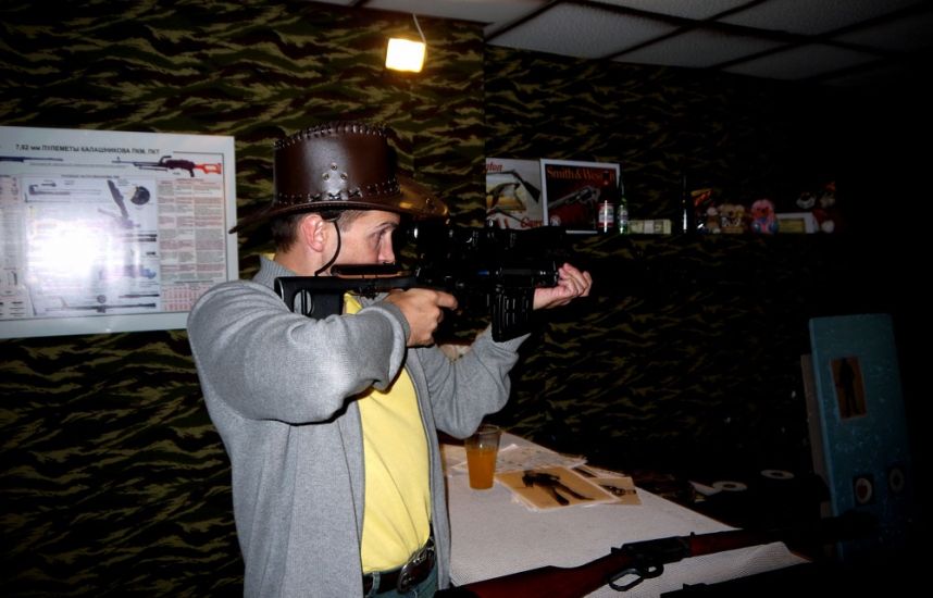 Посетитель целится из пневматического оружия под наблюдением инструктора в клубе Золотая пуля