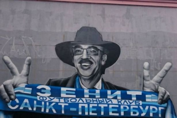 Известный артист изображен в черной шляпе, очках и шарфом с надписью «Футбольный клуб «Зенит» Санкт-Петербург» в руках.