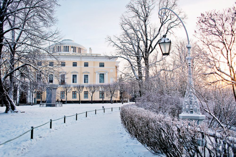 Павловский парк зимой с заснеженными деревьями, мостиком через реку Славянку и видом на Павловский дворец